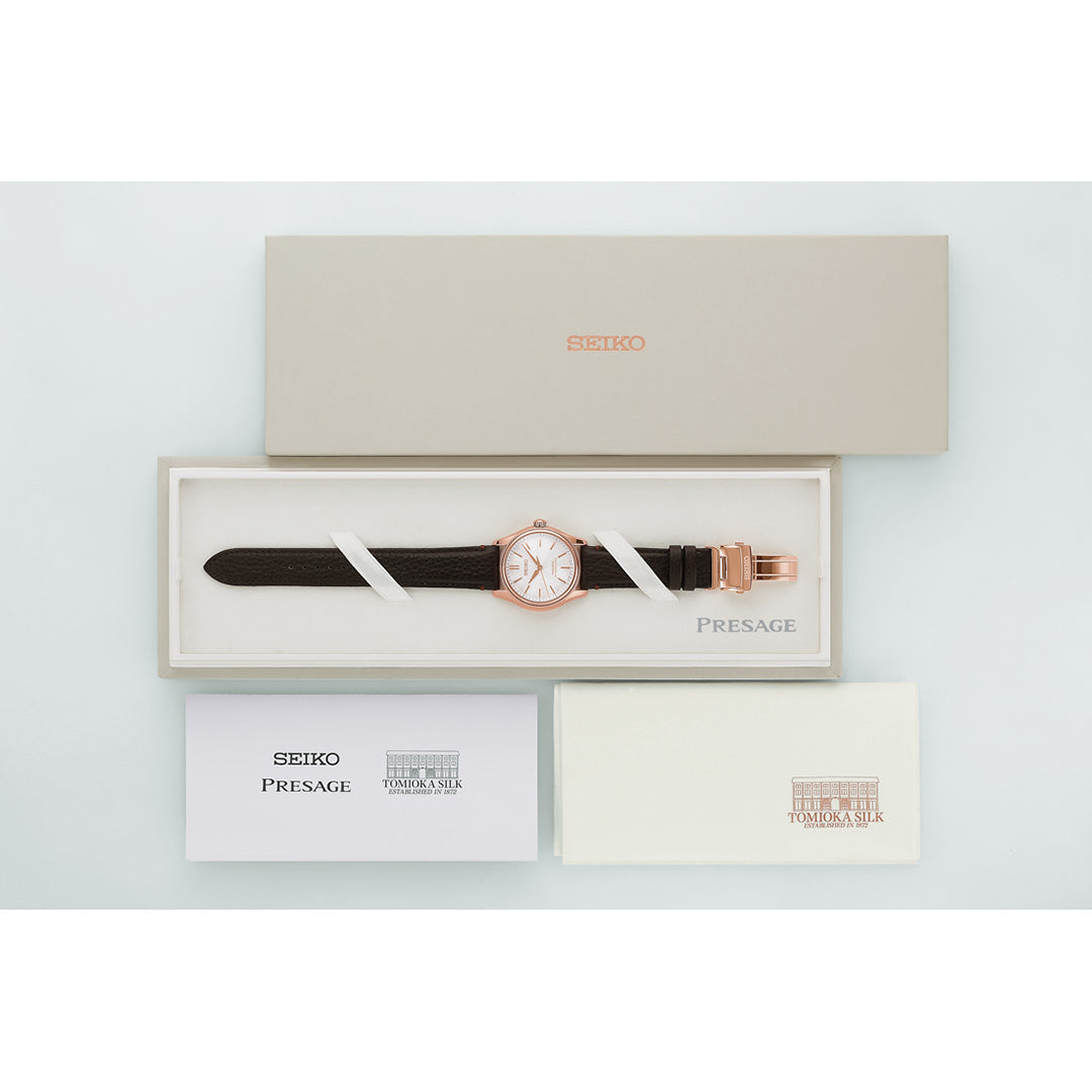 A Seiko Presage Classic Series Tomioka Silk Promotion Organization Automatic 38mm Watch Limited Edition of 2,000 pieces, featuring a brown strap, is elegantly displayed in a cream box alongside its lid and instruction booklets, all arranged on a white surface.