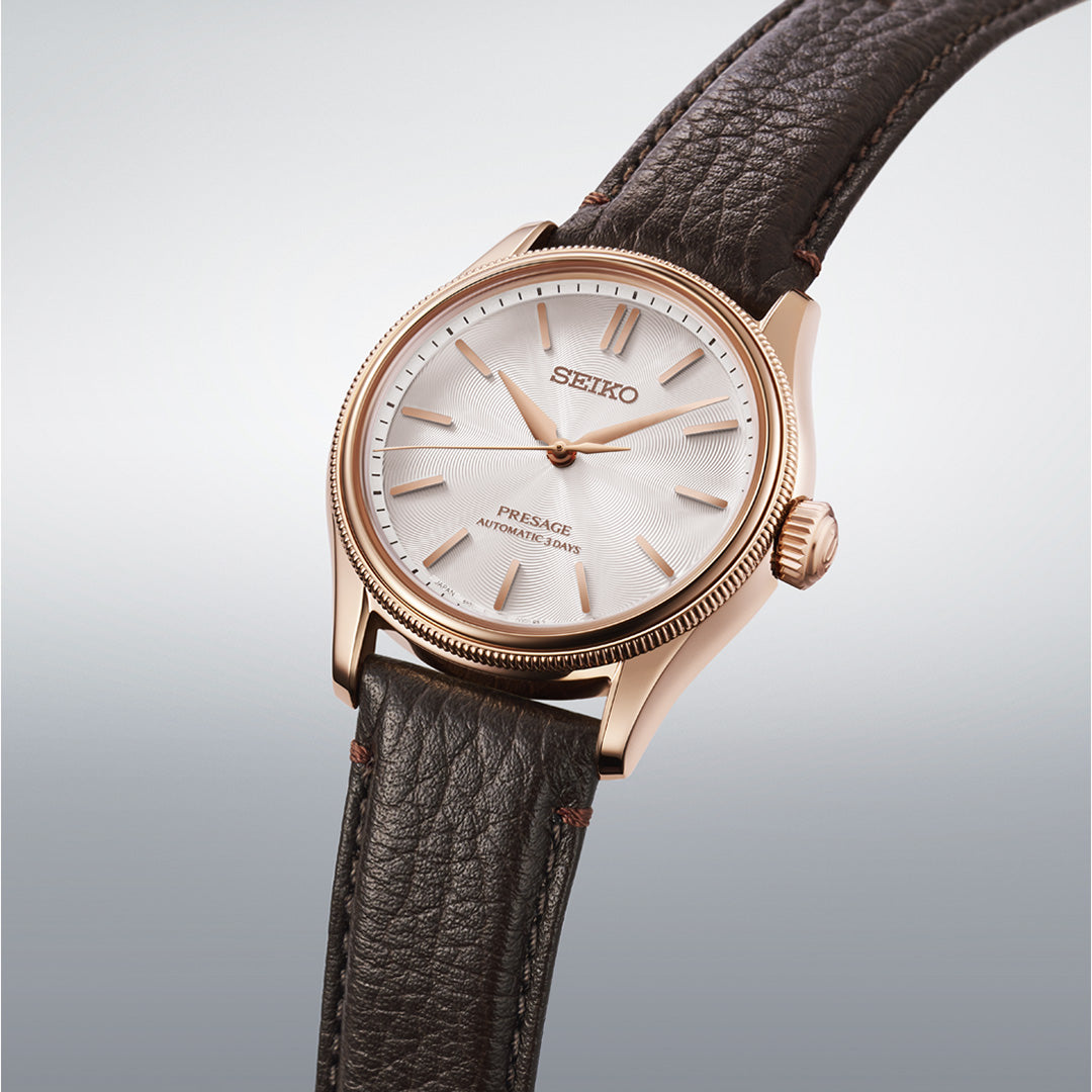 A Seiko Presage Classic Series Tomioka Silk Promotion Organization Automatic 38mm limited edition watch (one of only 2,000 pieces) featuring a rose gold case, textured white dial, and brown leather strap, displayed against a light gradient background.