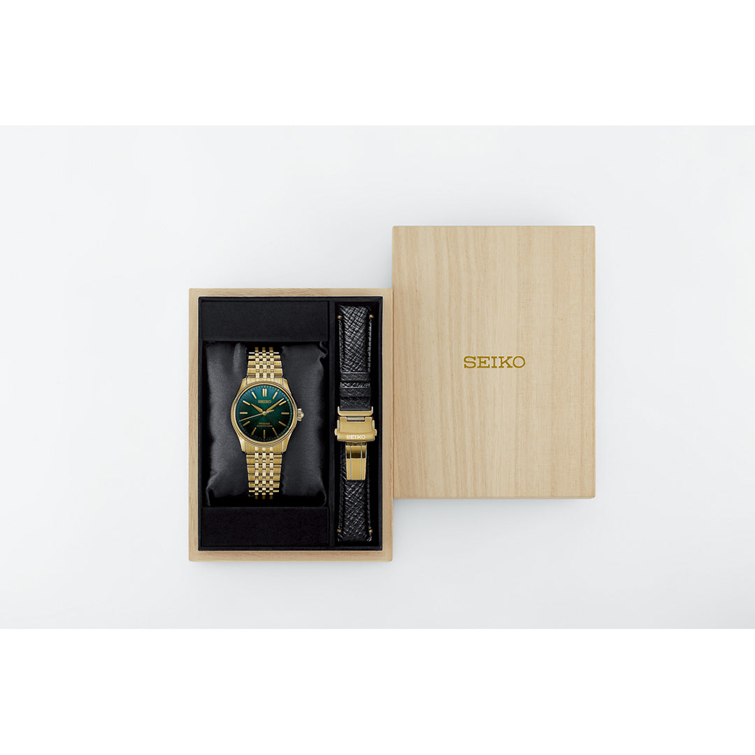 A Seiko Presage Classic Series Tradman’s Bonsai Automatic 38mm Watch, part of a limited edition of 2,000 pieces, is elegantly presented in a wooden box. The timepiece boasts a gold band and green dial. Accompanying it is a black leather strap with a gold buckle. The box lid bearing the “SEIKO” name rests beside the open display, highlighting this exclusive offering from Seiko.