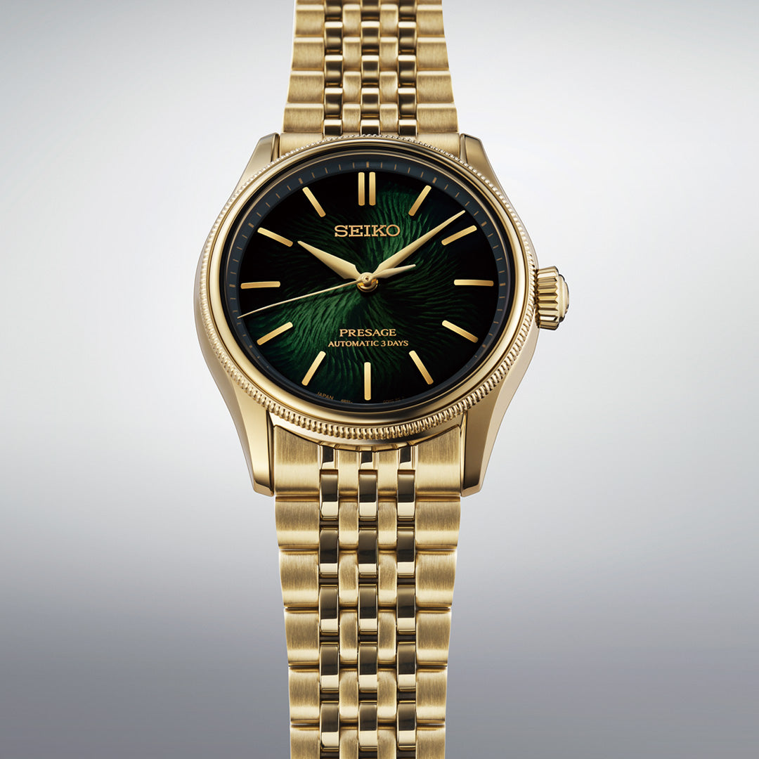 The Seiko Presage Classic Series Tradman’s Bonsai Automatic 38mm Watch, a limited edition of 2,000 pieces, is displayed against a plain light background. This gold wristwatch features a green and black dial, gold hour markers, and a metal link band.