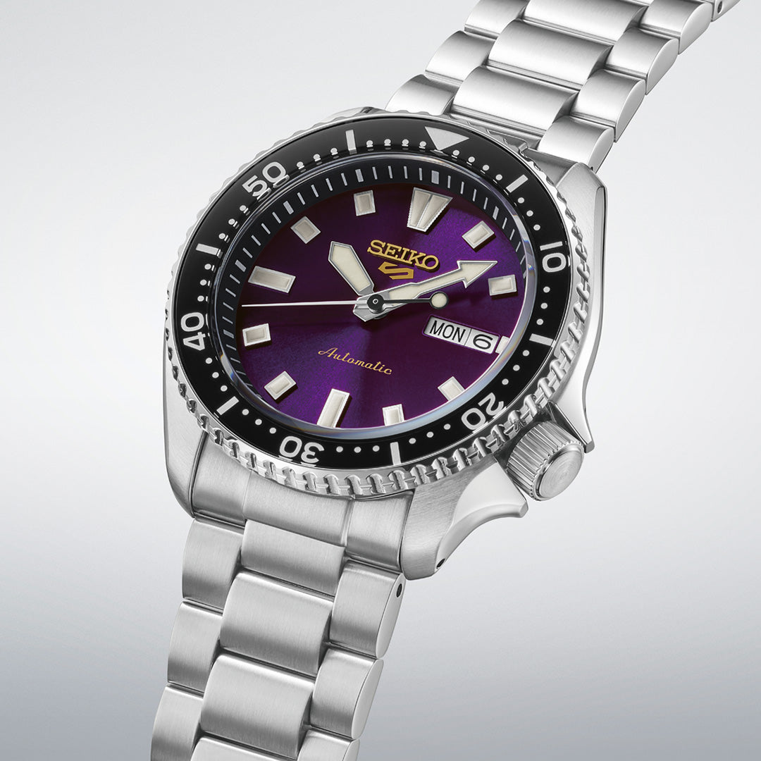The Seiko 5 Sports SKX Series Limited Edition Automatic 42.5mm Watch features a stainless steel case, a striking metallic purple dial with bold hour markers, a black bezel, and a silver band. This Seiko timepiece also displays both the day and date.