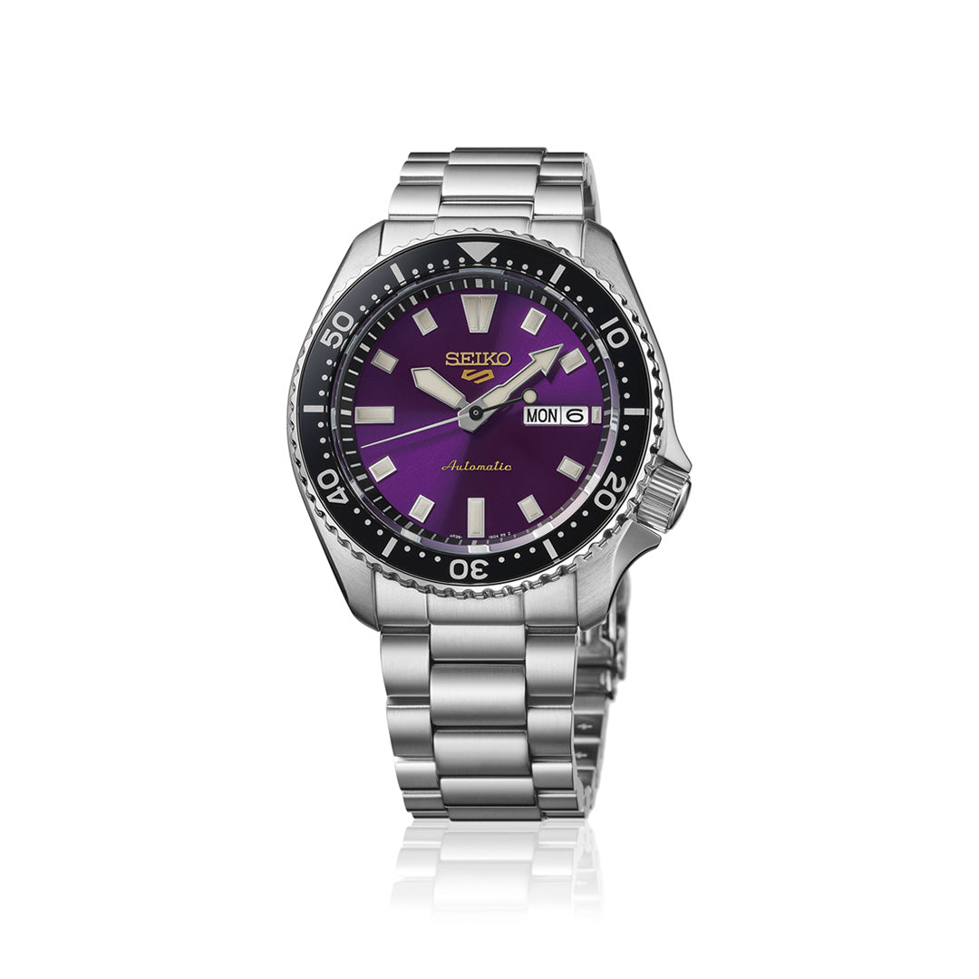 The Seiko 5 Sports SKX Series Limited Edition Automatic 42.5mm Watch features a stainless steel case, a striking purple dial with silver indices, and a day-date window showing “MON 6”. Its bezel is marked with minute gradations, and it comes with a classic metal link strap.