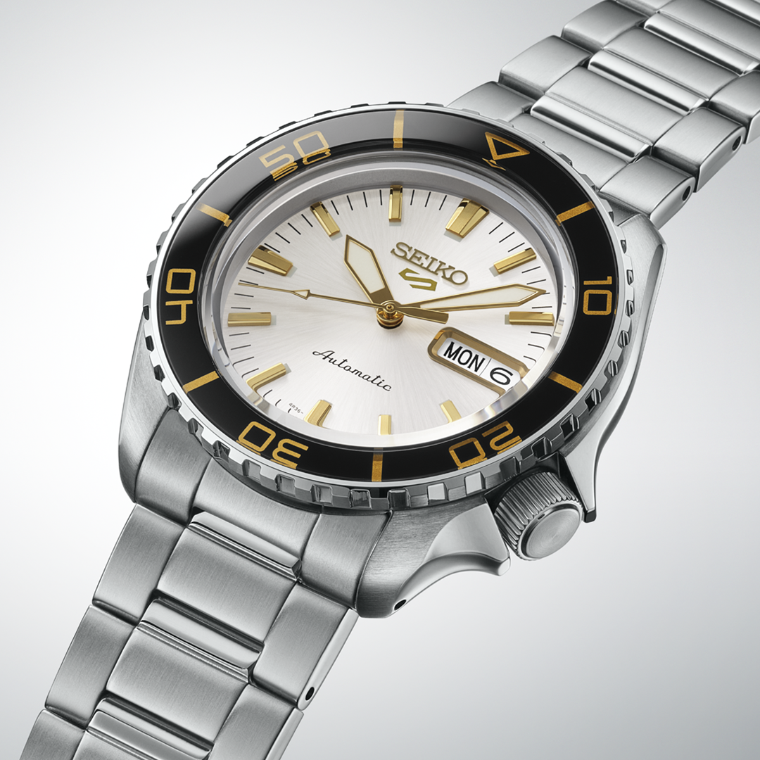 Seiko 5 Sports SKX Series Automatic 42.5mm Watch featuring a silver dial, gold-toned indices and hands, a black rotating bezel with gold numerals, and a stainless steel link bracelet.
