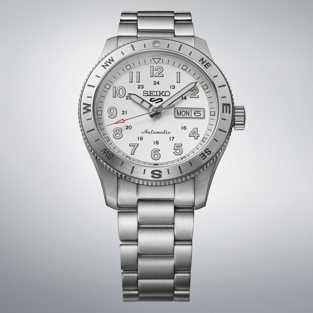 The Seiko 5 Sports Field Series Automatic 41mm Watch by Seiko features a silver dial with numbered hour markers, a metal bracelet, LumiBrite hands for enhanced visibility, a day-date display, and compass directions on the bezel.