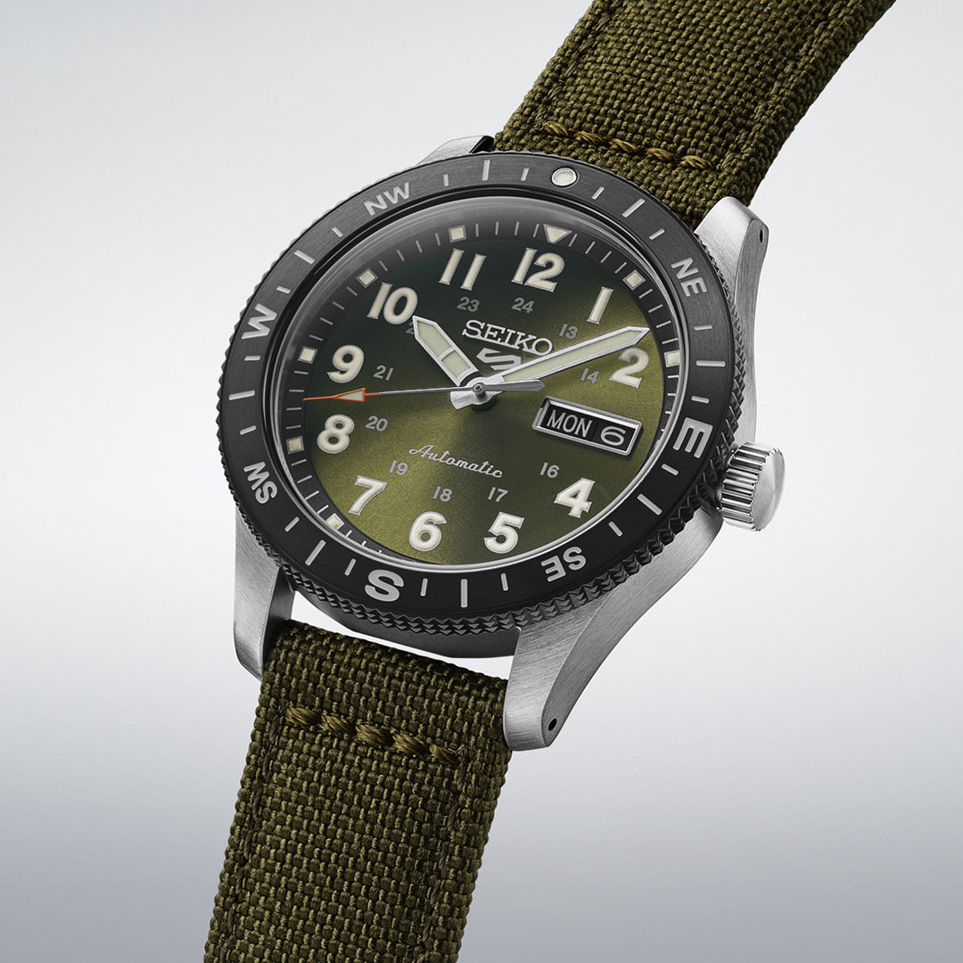 The Seiko 5 Sports Field Series Automatic 41mm Watch by Seiko features a durable green nylon strap, a black rotating bezel with compass markings, and a day-date display. It is enhanced with LumiBrite hands and markers set against a light gray dial.