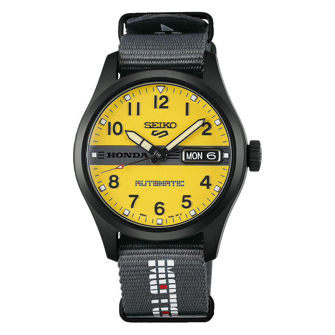 The Seiko 5 Sports Field Series MOTOCOMPO Limited Edition Automatic 36.37mm watch features a yellow dial, black case, day-date window, black bezel, and distinctive “Honda” branding. It comes with a black and gray fabric strap accented by white and red stitching.