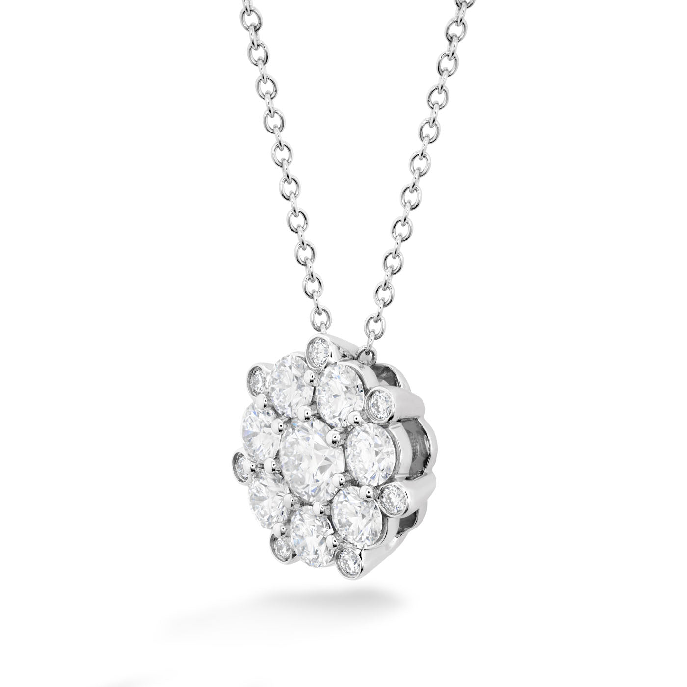 A close-up of the Hearts On Fire Beloved 18K White Gold Diamond Cluster Pendant showcases a stunning arrangement of multiple small round diamonds in a floral pattern. This exquisite pendant from Hearts on Fire hangs gracefully on a delicate chain against a white background.