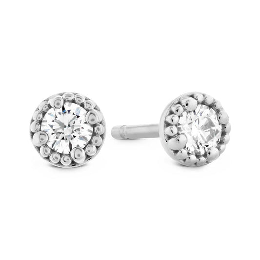 The Hearts On Fire Liliana Milgrain Stud Earrings feature a pair of exquisite silver studs, each accented with a round, sparkling gemstone at the center. These earrings are elegantly surrounded by a decorative border of small metallic beads, adding an exquisite touch.