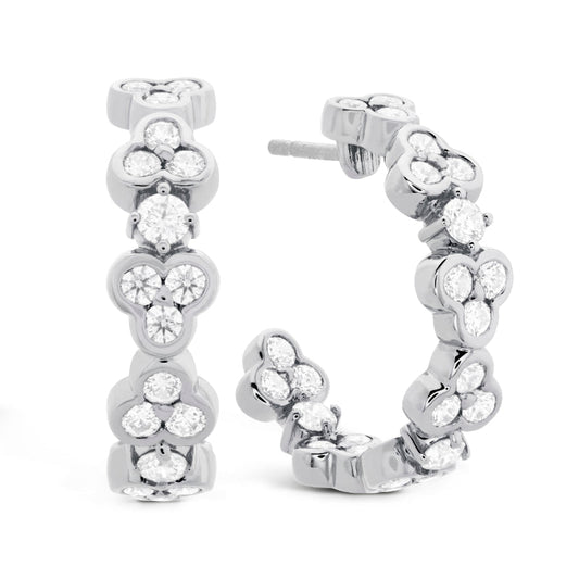 The Hearts On Fire Effervescence Hoop Earrings by Hearts on Fire are elegant pieces crafted from white gold, showcasing intricate floral cluster designs adorned with sparkling round diamonds. These luxurious jewelry items are beautifully displayed standing upright against a white background.
