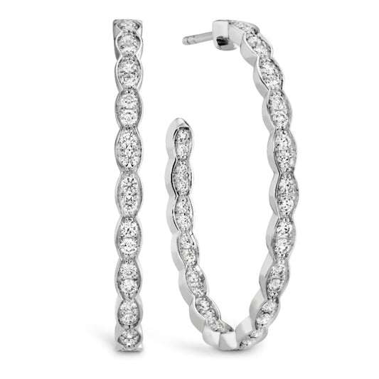 The Hearts On Fire Lorelei Floral Oval Inside-Out Hoop Earrings feature a twisted design encrusted with sparkling round diamonds. These exquisite luxury jewelry pieces from Hearts on Fire are positioned upright, showcasing their detailed craftsmanship against a plain white background.