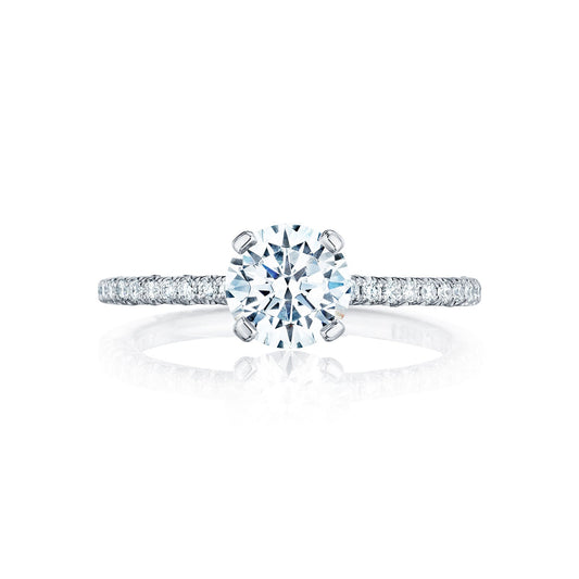 The Tacori Petite Crescent 18K White Gold Round Brilliant Solitaire Semi Mount Engagement Ring features a large round diamond at its center. This engagement ring, crafted by the skilled gemologists at Tacori, is designed in the Petite Crescent style with a band adorned with smaller diamonds that create a sparkling effect against a white background.