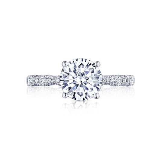 This Tacori Petite Crescent engagement ring in 18K white gold showcases a round brilliant cut diamond set in a classic four-prong design, enhanced by French pavé-set diamonds. The band, adorned with smaller diamonds and intricate detailing, exudes elegance and sophistication.