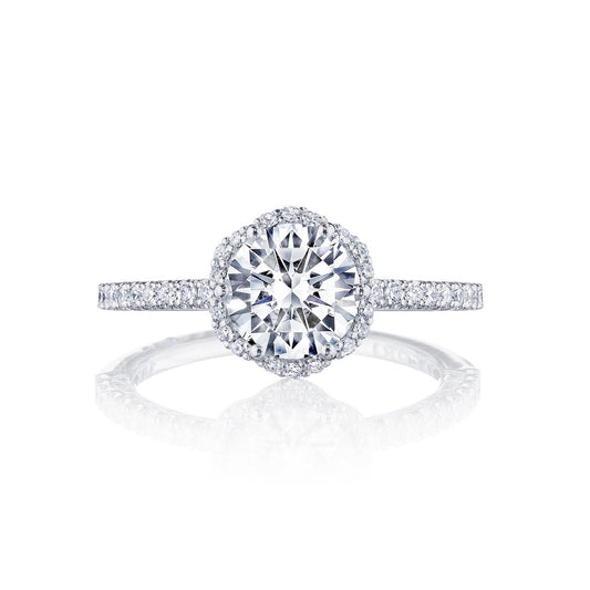 The Tacori Petite Crescent 18K White Gold Round Brilliant Semi Mount with Diamond Band and Halo Engagement Ring is showcased against a white background. Carefully crafted by Tacori gemologists, this ring embodies elegance and timeless allure with its large round center stone surrounded by pave-set diamonds on a slim band, also adorned with diamonds.