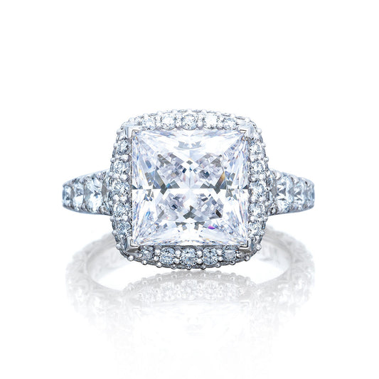 The Tacori Petite Crescent RoyalT Platinum Princess Semi Mount with Diamond Band and Halo Engagement Ring by Tacori highlights a prominent princess-cut diamond at its center, surrounded by a halo of smaller, round diamonds. The band is embellished with more diamonds, contributing to the ring's shimmering and sophisticated design on a reflective white surface.