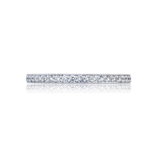 A Tacori RoyalT Sculpted Crescent Platinum Round Brilliant Pavé Diamond Anniversary Ring, featuring a thin silver band encrusted with small, sparkling diamonds, is set against a white background. The ring reflects light, casting a delicate shadow beneath it.