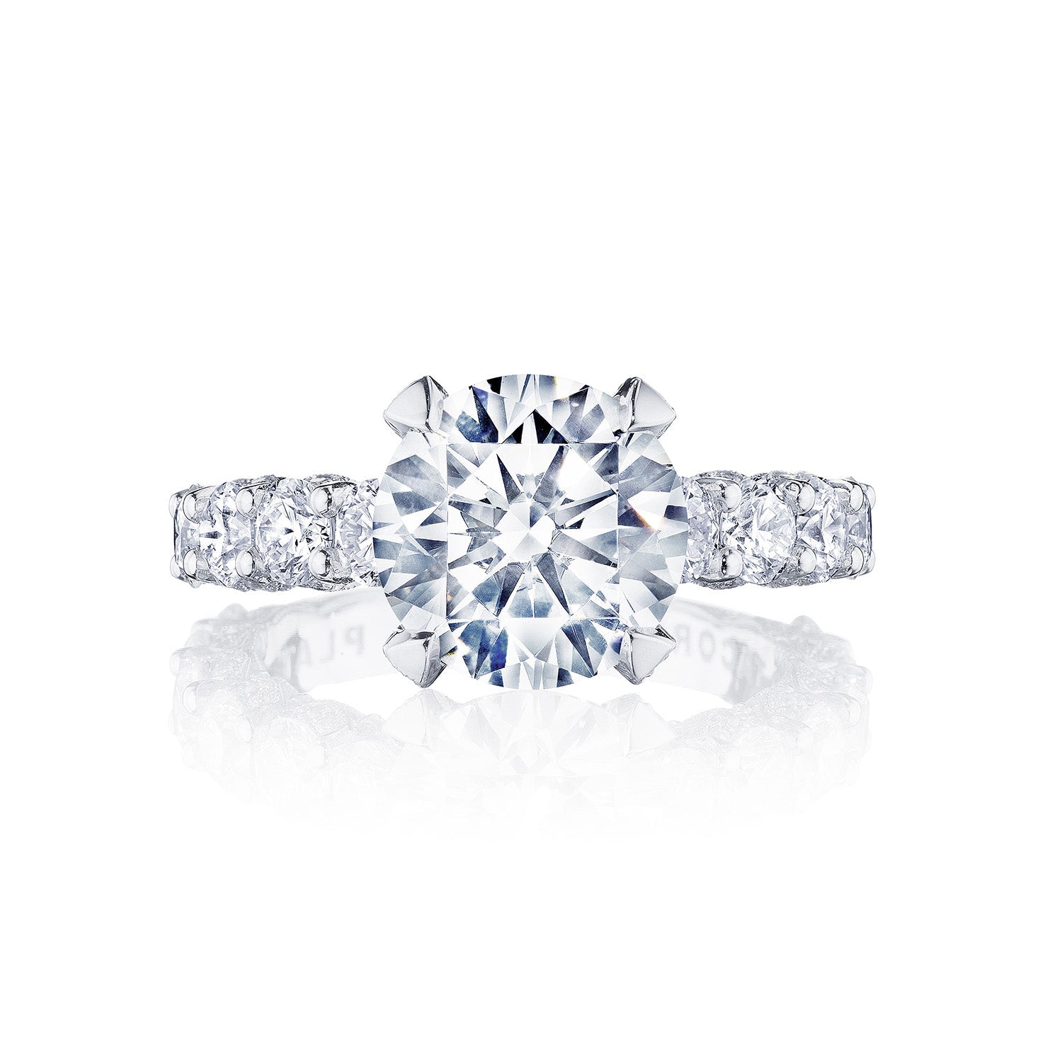 The Tacori Classic Crescent RoyalT Platinum Round Brilliant Solitaire Semi Mount with Diamond Band Engagement Ring features a dazzling round center stone set in a prong setting. Expertly crafted by Tacori, the band is adorned with smaller diamonds that enhance its brilliance and elegance. The ring is presented against a white background with a reflective surface.