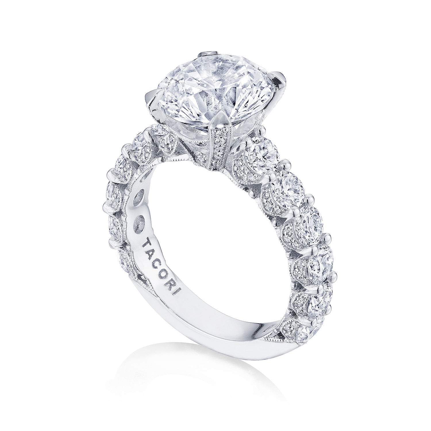This Tacori Classic Crescent RoyalT engagement ring is crafted from platinum and features a stunning round brilliant solitaire centerpiece. Complemented by exquisite diamond studding along the band, its intricate designs highlight the brilliance of the stones. The brand name "Tacori" is engraved on the band, symbolizing the artistry of Tacori gemologists.
