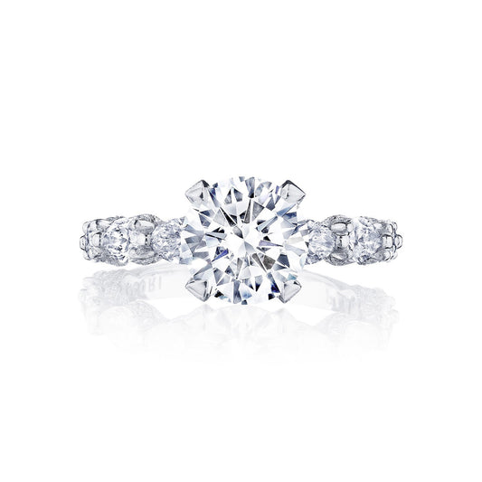 The Tacori Classic Crescent RoyalT Platinum Round Brilliant Solitaire Semi Mount with Diamond Band Engagement Ring showcases a spectacular engagement ring design, featuring a large, round center stone. Designed by Tacori gemologists, the platinum band is adorned with smaller diamonds on either side, adding to its elegance and brilliance.