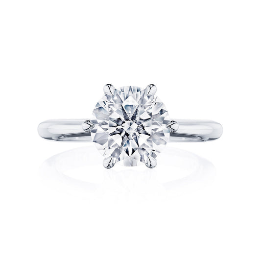 The Tacori Founder's Collection RoyalT engagement ring showcases a brilliant round-cut diamond solitaire set in a six-prong setting. The polished and sleek band with diamond accents amplifies the gemstone's sparkle, with the image capturing its elegance from a front view on a white background.