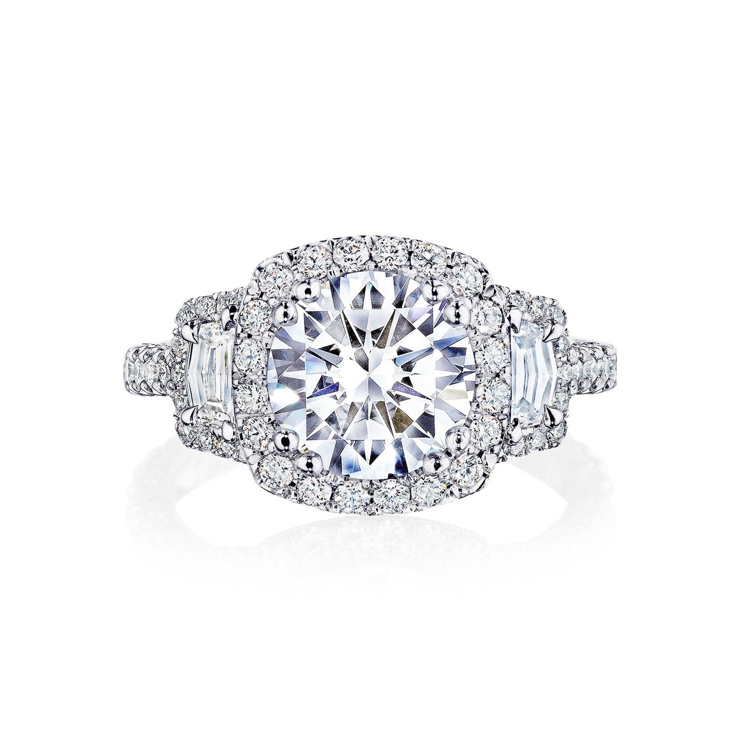The Tacori Petite Crescent Royal T Platinum Round Brilliant Three Stone Halo Semi Mount with Diamond Side Stone Engagement Ring is meticulously crafted by Tacori gemologists. Featuring a large round center stone encircled by a halo of smaller diamonds, the band also includes additional diamonds and a geometric motif, adding to its intricate design. The ring is showcased against a white background.