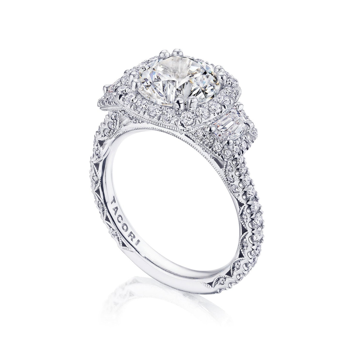 The Tacori Petite Crescent Royal T Platinum Round Brilliant Three Stone Halo Semi Mount with Diamond Side Stone Engagement Ring showcases a large round diamond centerpiece and is expertly crafted by Tacori gemologists. It features smaller diamonds on an intricate band adorned with delicate filigree and embellishments.