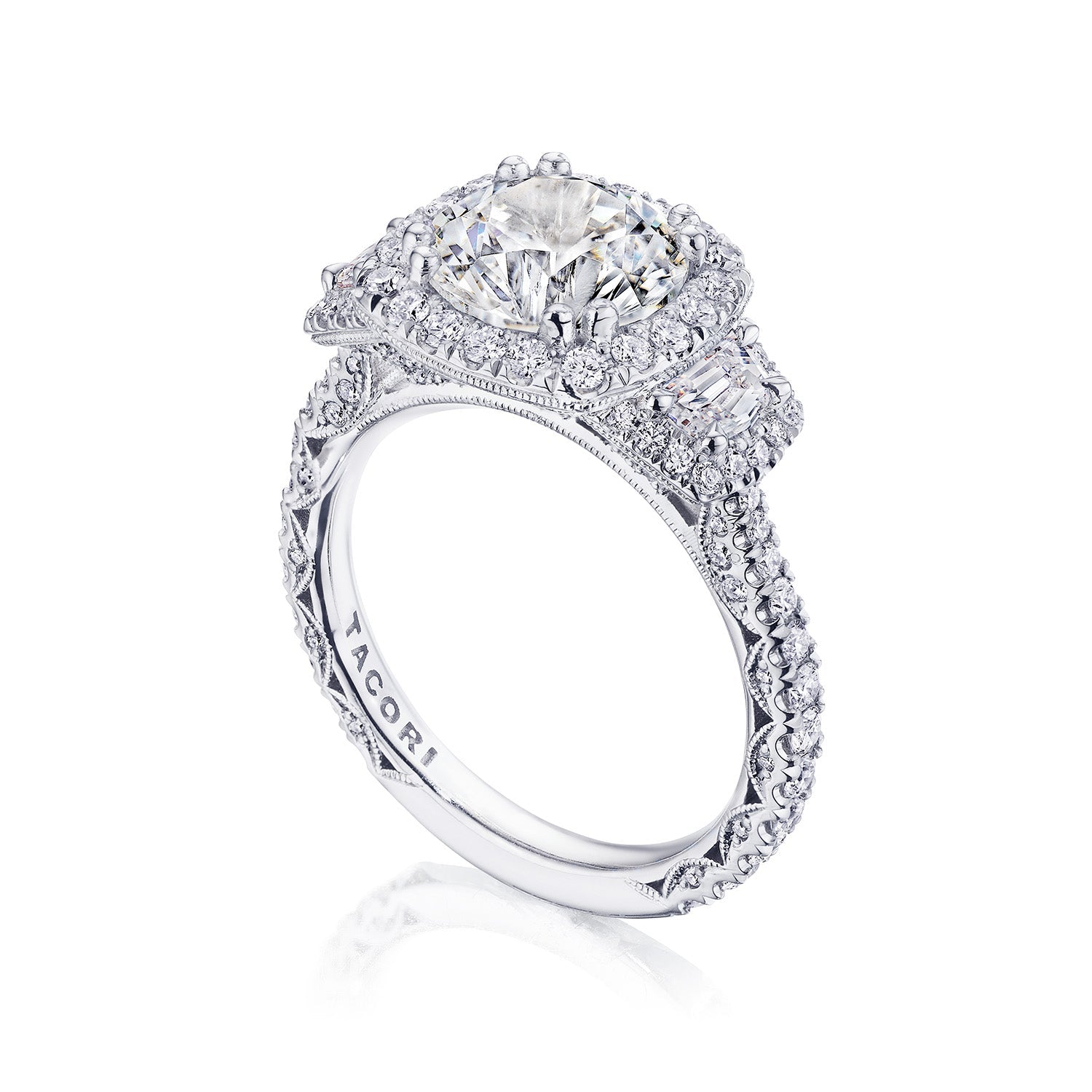 The Tacori Petite Crescent Royal T Platinum Round Brilliant Three Stone Halo Semi Mount with Diamond Side Stone Engagement Ring showcases a large round diamond centerpiece and is expertly crafted by Tacori gemologists. It features smaller diamonds on an intricate band adorned with delicate filigree and embellishments.