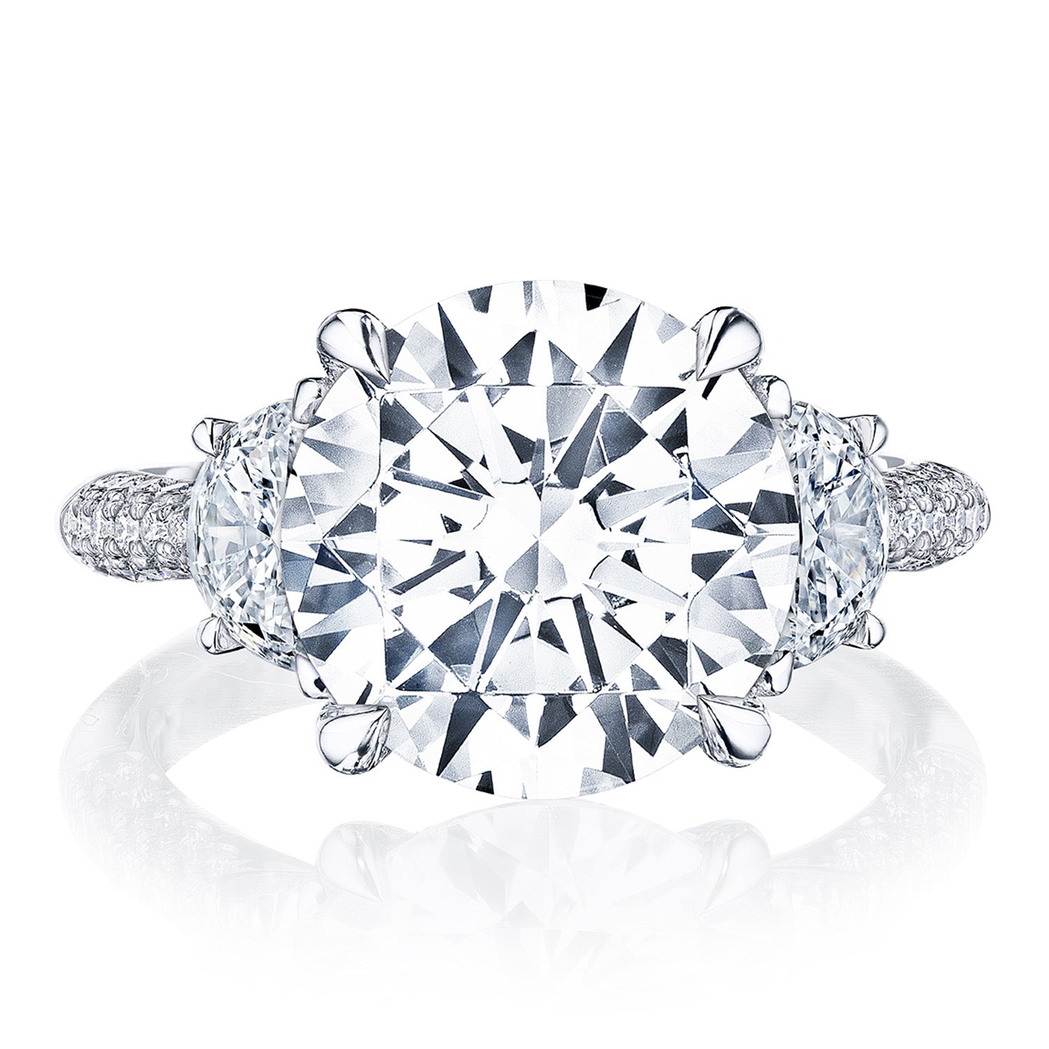The Tacori Founder's Collection RoyalT Platinum Round Brilliant Three Stone Semi Mount with Diamond Side Stone Engagement Ring by Tacori showcases a close-up of its exquisite design. It features a large, round diamond in a four-prong setting. The band is elegantly adorned with pavé diamonds and flanked by two half-moon diamonds, reflecting a brilliant sparkle that enhances the allure of this engagement ring.
