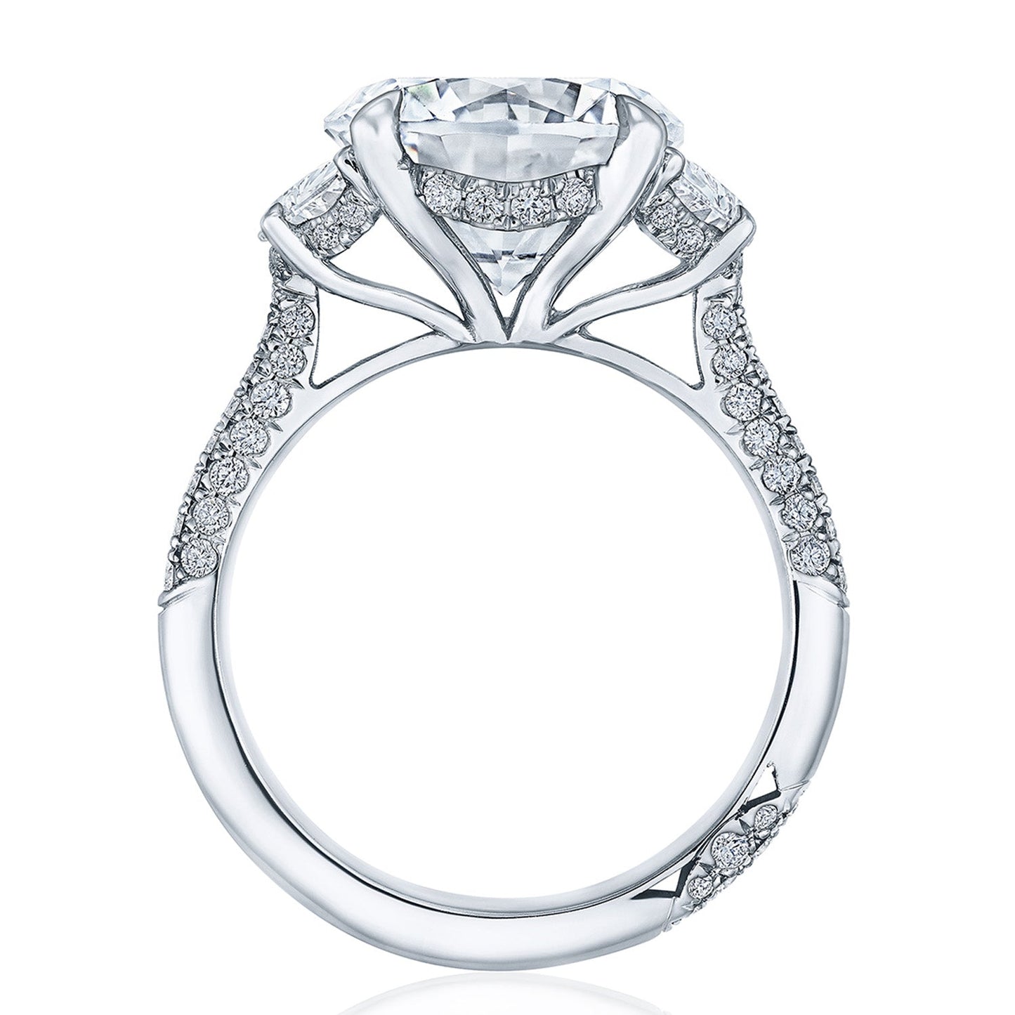 A close-up of the Tacori Founder's Collection RoyalT Platinum Round Brilliant Three Stone Semi Mount with Diamond Side Stone Engagement Ring showcases its luxurious design featuring a large central diamond in a detailed setting. The band is adorned with pavé diamonds, exemplifying Tacori's fine craftsmanship and elegance.