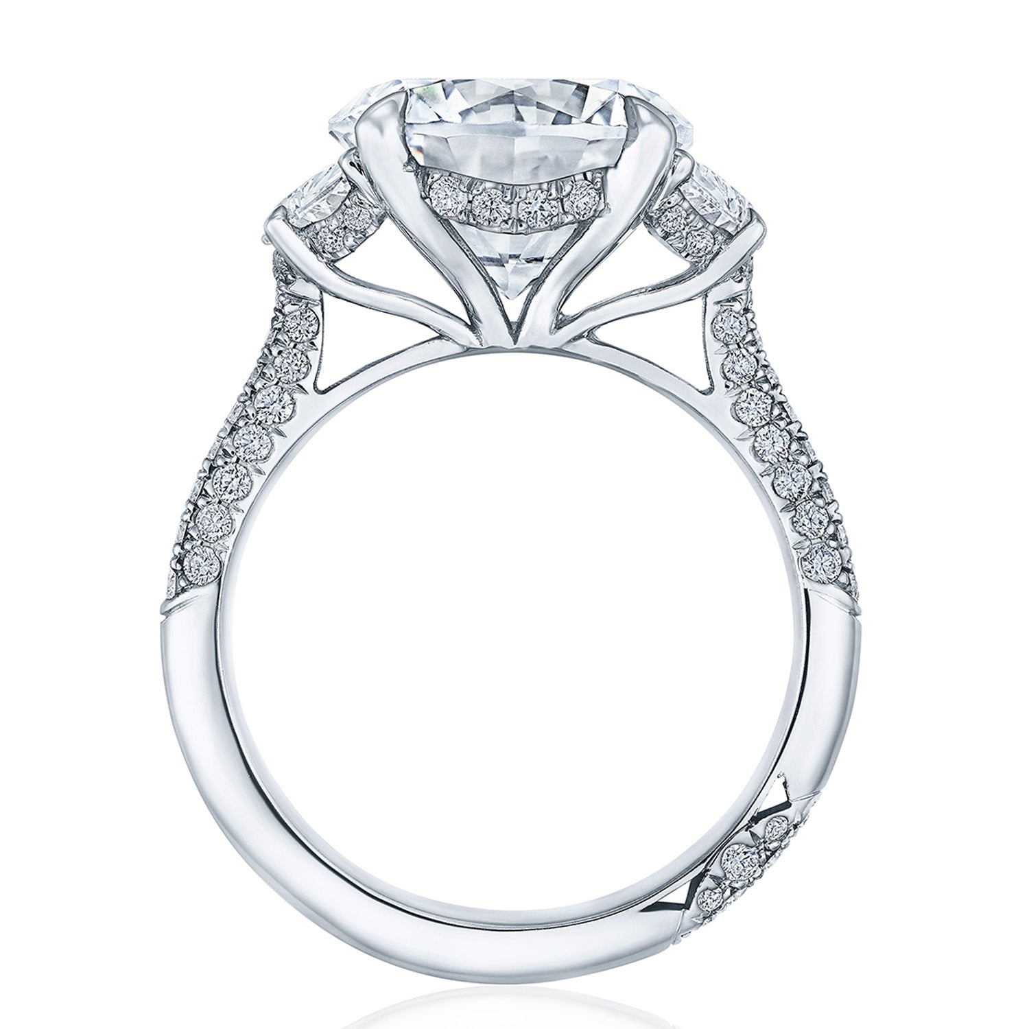 A close-up of the Tacori Founder's Collection RoyalT Platinum Round Brilliant Three Stone Semi Mount with Diamond Side Stone Engagement Ring showcases its luxurious design featuring a large central diamond in a detailed setting. The band is adorned with pavé diamonds, exemplifying Tacori's fine craftsmanship and elegance.