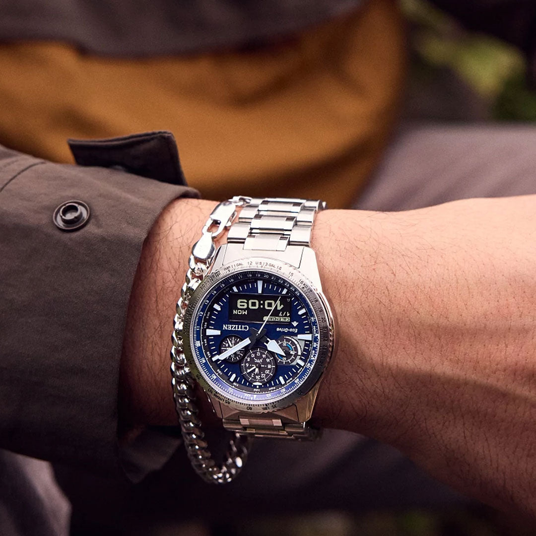 A close-up shows a person wearing a CITIZEN Promaster Skyhawk U830 Eco-Drive 43mm stainless steel watch with a blue and black analog-digital dial and silver bracelet, paired with an olive-green jacket.