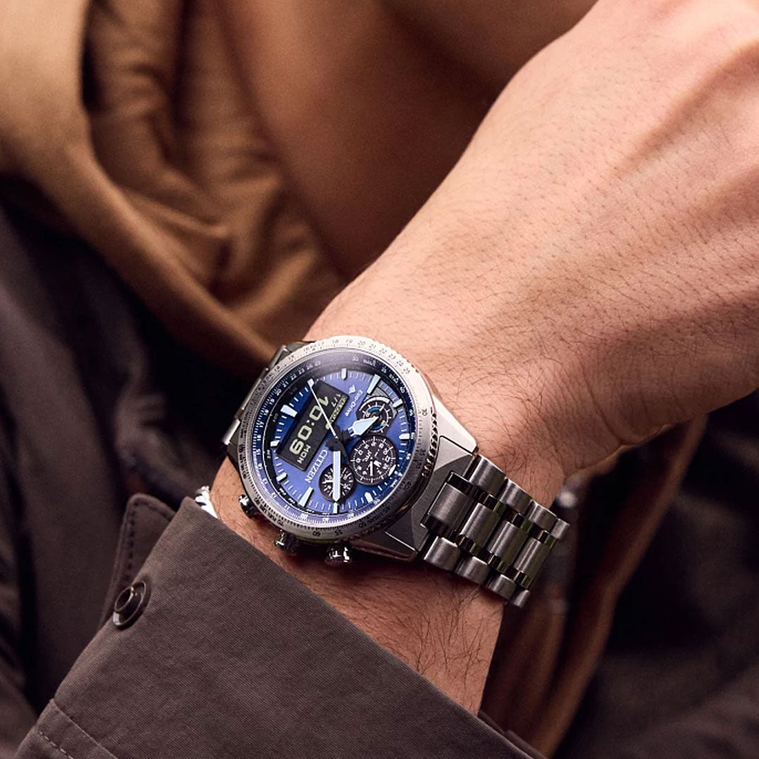 A person wears the CITIZEN Promaster Skyhawk U830 Eco-Drive 43mm stainless steel watch with a blue dial and multiple subdials on their left wrist, complementing their brown jacket and tan scarf.
