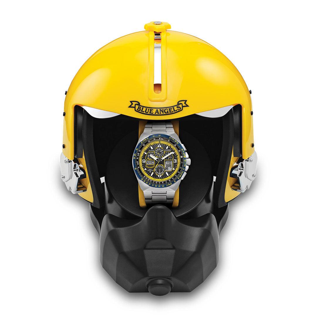 The CITIZEN Promaster Skyhawk A-T Eco-Drive 46mm Watch is shown in a yellow and black pilot-style helmet labeled "Blue Angels" above the visor, highlighting the watch’s silver and blue design and durable build.