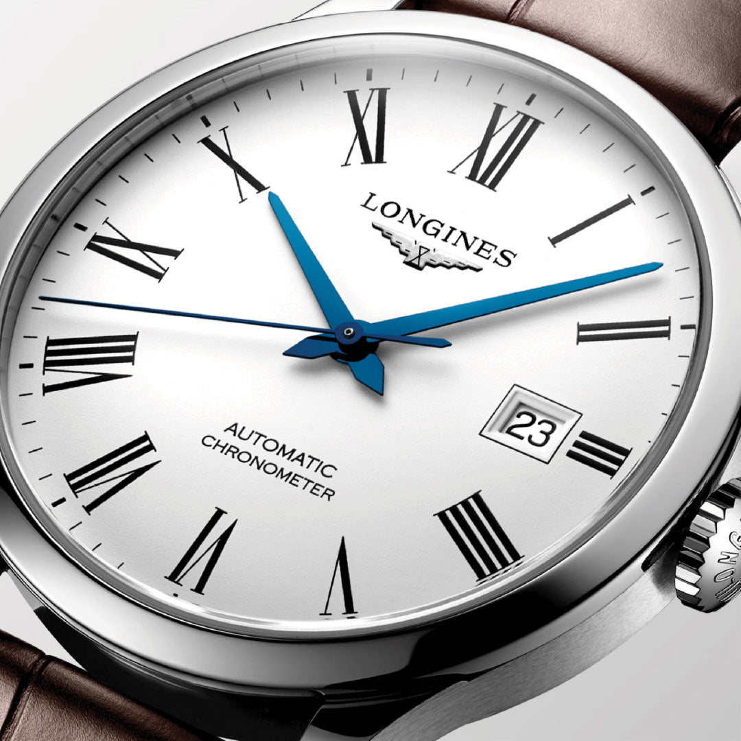 Close-up of the Longines Record Automatic 40mm Watch, showcasing its classic elegance with a silver dial adorned with Roman numerals, blue hour and minute hands, and a date display at 3 o'clock. It features a brown leather strap and proudly displays "Automatic Chronometer," complete with a single-crystal silicon balance spring.