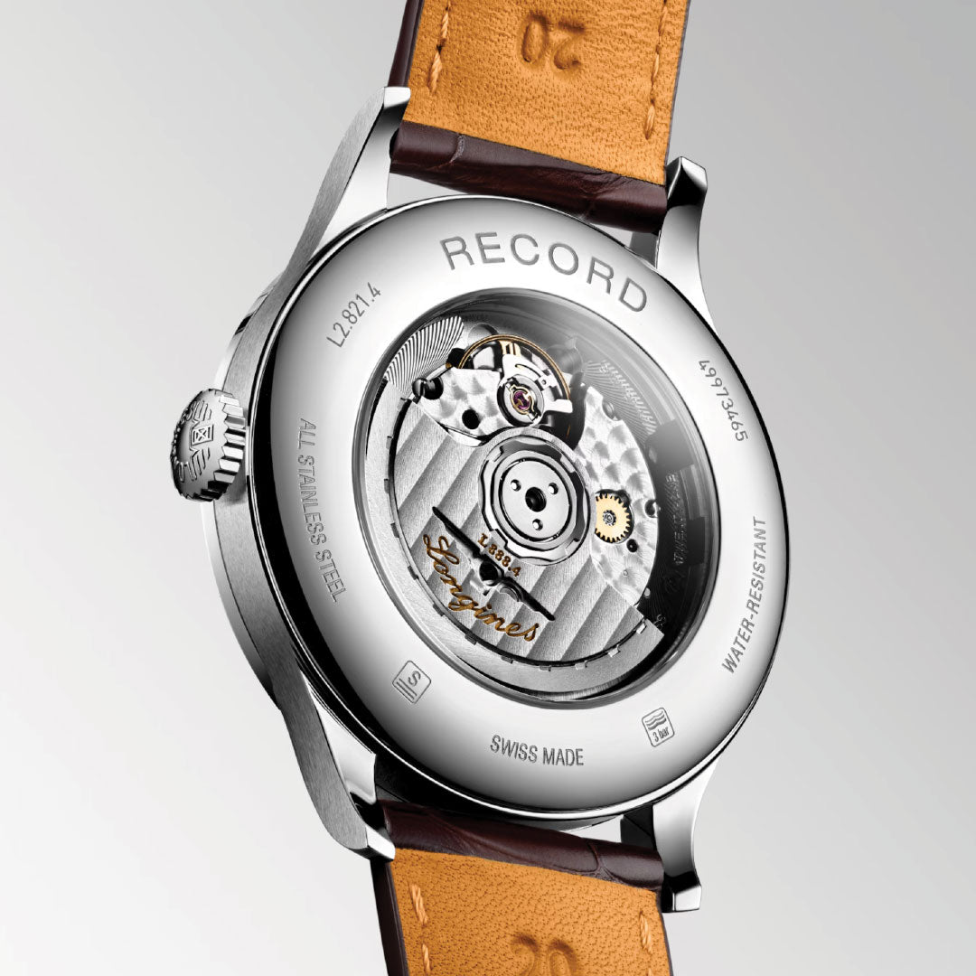 The image showcases the back of a Longines Record Automatic 40mm watch, highlighting its intricate mechanical movement with a single-crystal silicon balance spring visible through an open case. This Swiss-made timepiece features a stainless steel body and a brown leather strap, beautifully engraved with "Chronometer.