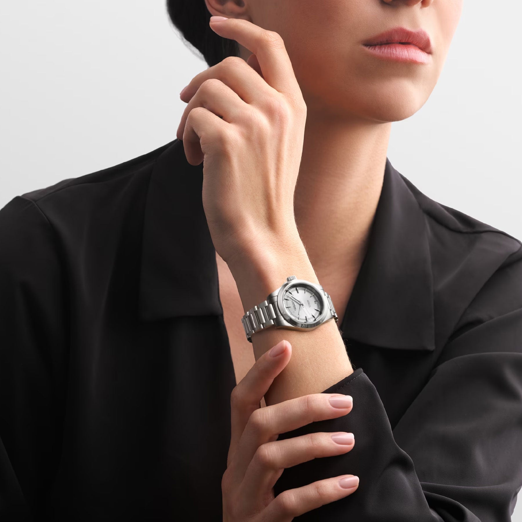 A person in a black shirt elegantly showcases a Longines Conquest Automatic 34mm Watch with a white dial. The raised arm highlights the watch's performance against a neutral background, merging elegance and precision in a minimalistic scene.