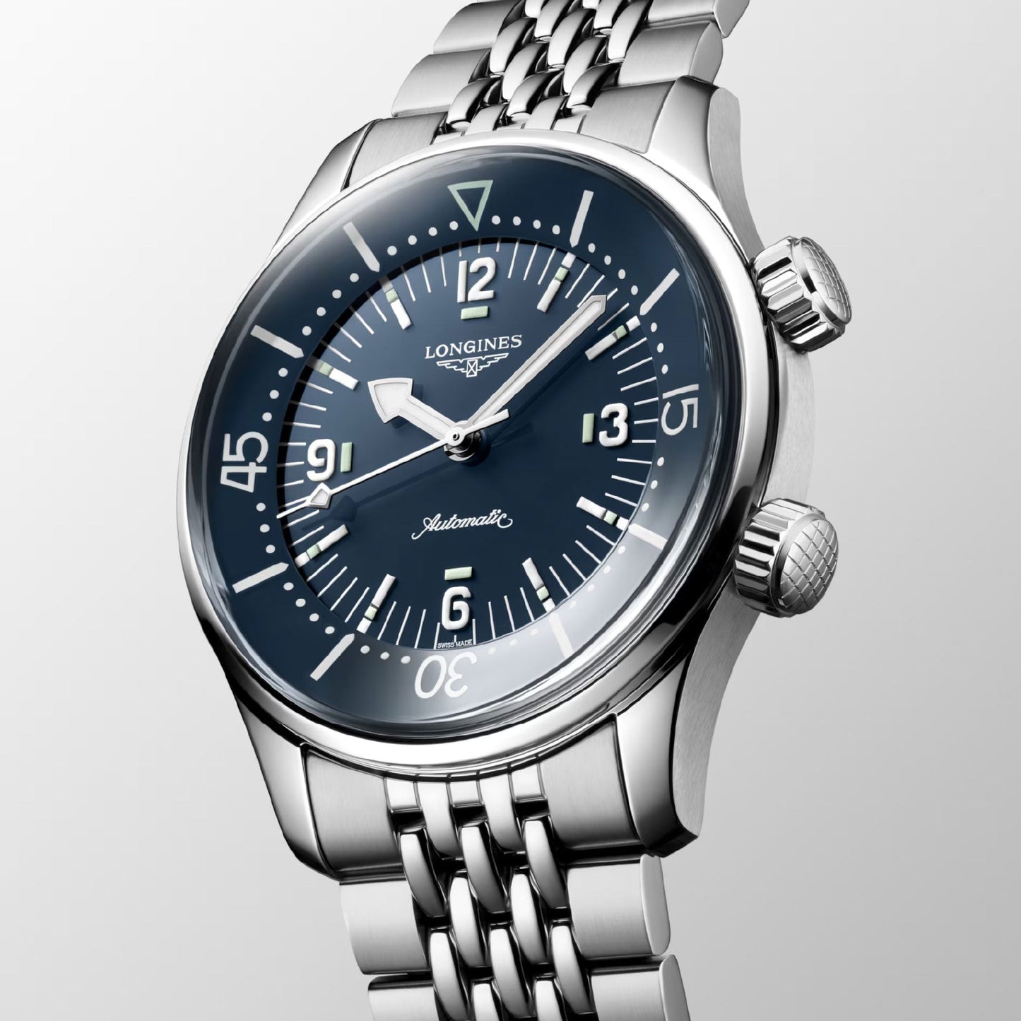 The Longines Legend Diver Automatic 39mm Watch features a striking navy blue dial adorned with large white numerals, luminescent hands, and an elegant silver metal link band. Echoing the iconic style of the Longines brand, this timepiece stands out against a light grey backdrop.