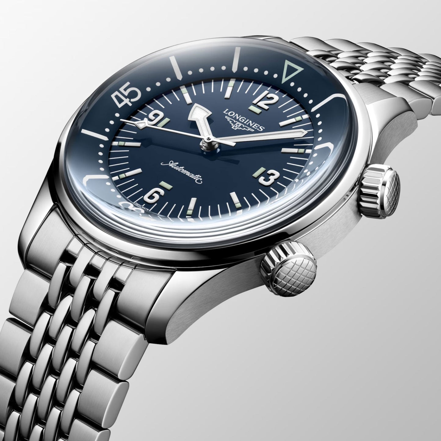 The Longines Legend Diver Automatic 39mm Watch by Longines is a silver wristwatch with a polished metal bracelet and a blue dial. It features large numerals, an automatic movement label, and two distinct crowns. This classic diver's watch is elegantly angled against a neutral background.