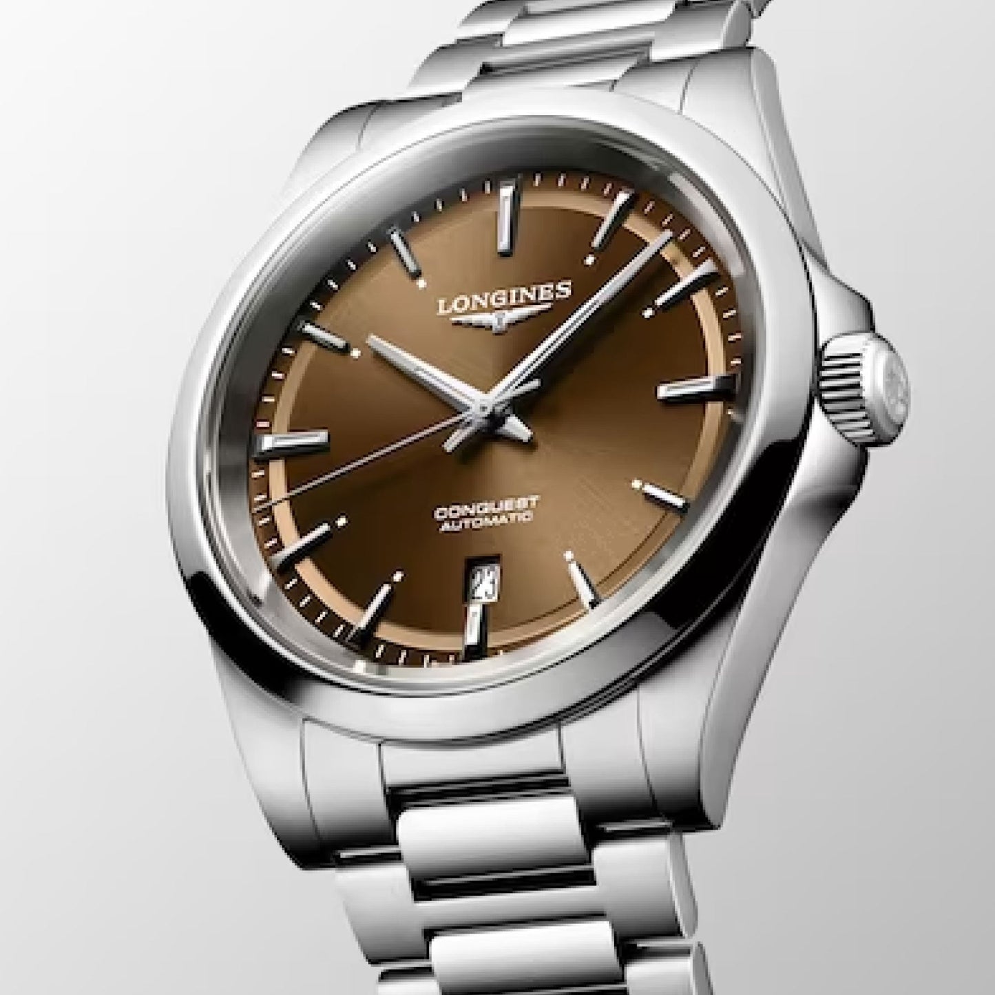 The Longines Conquest Automatic 41mm Watch by Longines features a brown dial adorned with silver hour markers and comes paired with a stainless steel bracelet. It includes a date display, while its polished metal case and textured crown are elegantly showcased against a subtle gradient background, embodying timeless sophistication.