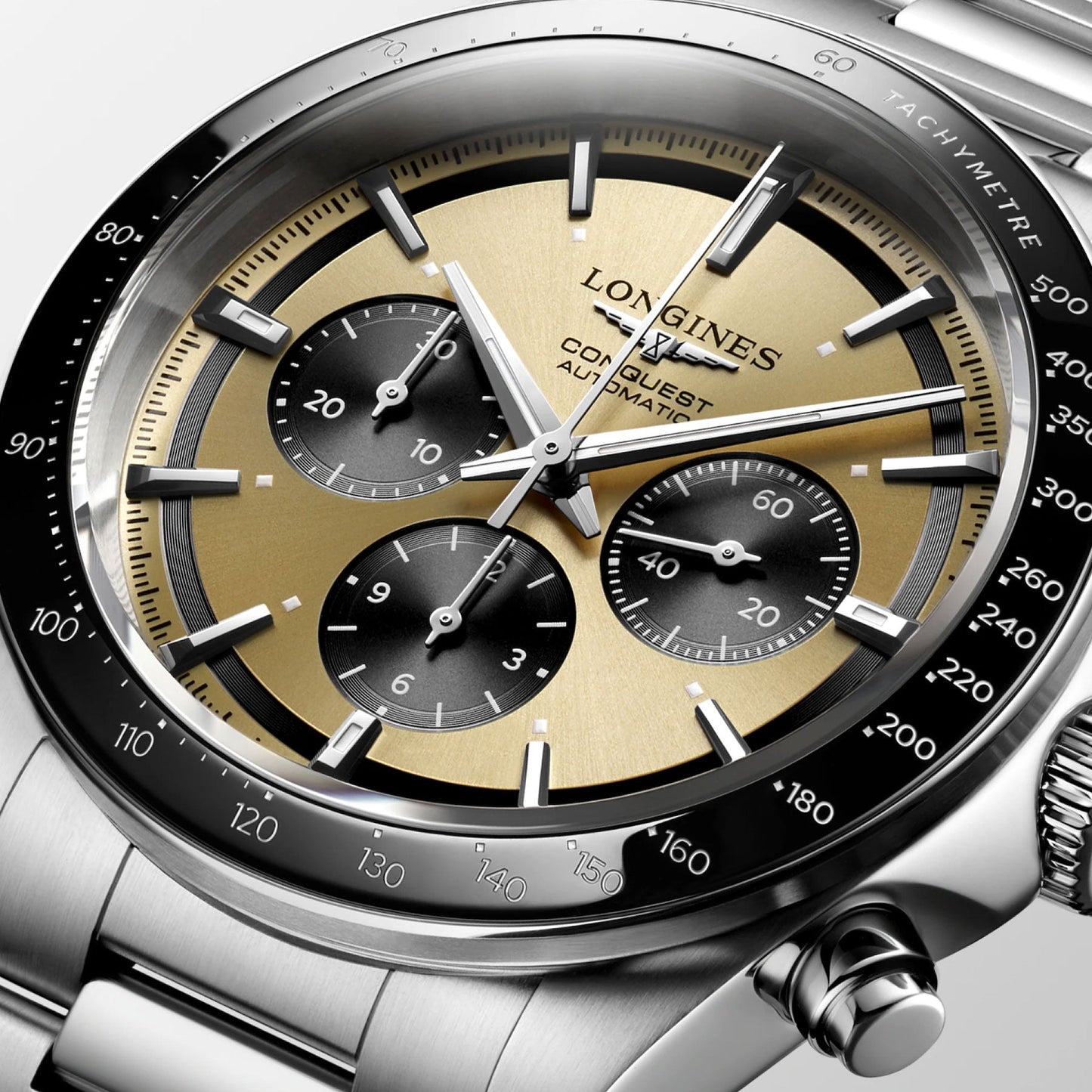 Close-up of the sophisticated Longines Conquest Automatic 42mm Watch. It showcases a gold and black dial with three sub-dials, silver hour markers, and a stainless steel bracelet. The tachymeter scale is prominently displayed on the bezel.