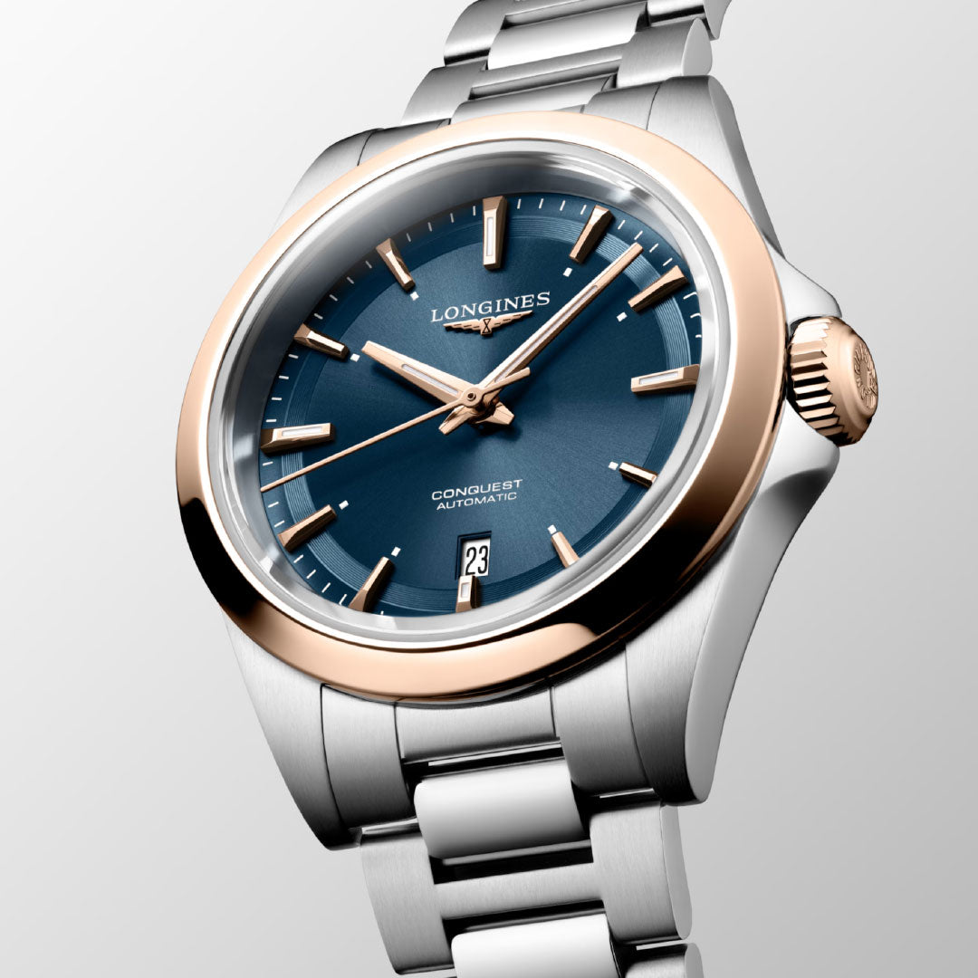 The Longines Conquest Automatic 30mm Watch features a blue dial, gold bezel, and two-tone bracelet—blending sporty elegance and everyday practicality. Silver markers and a date display at 6 o’clock complete its refined design.