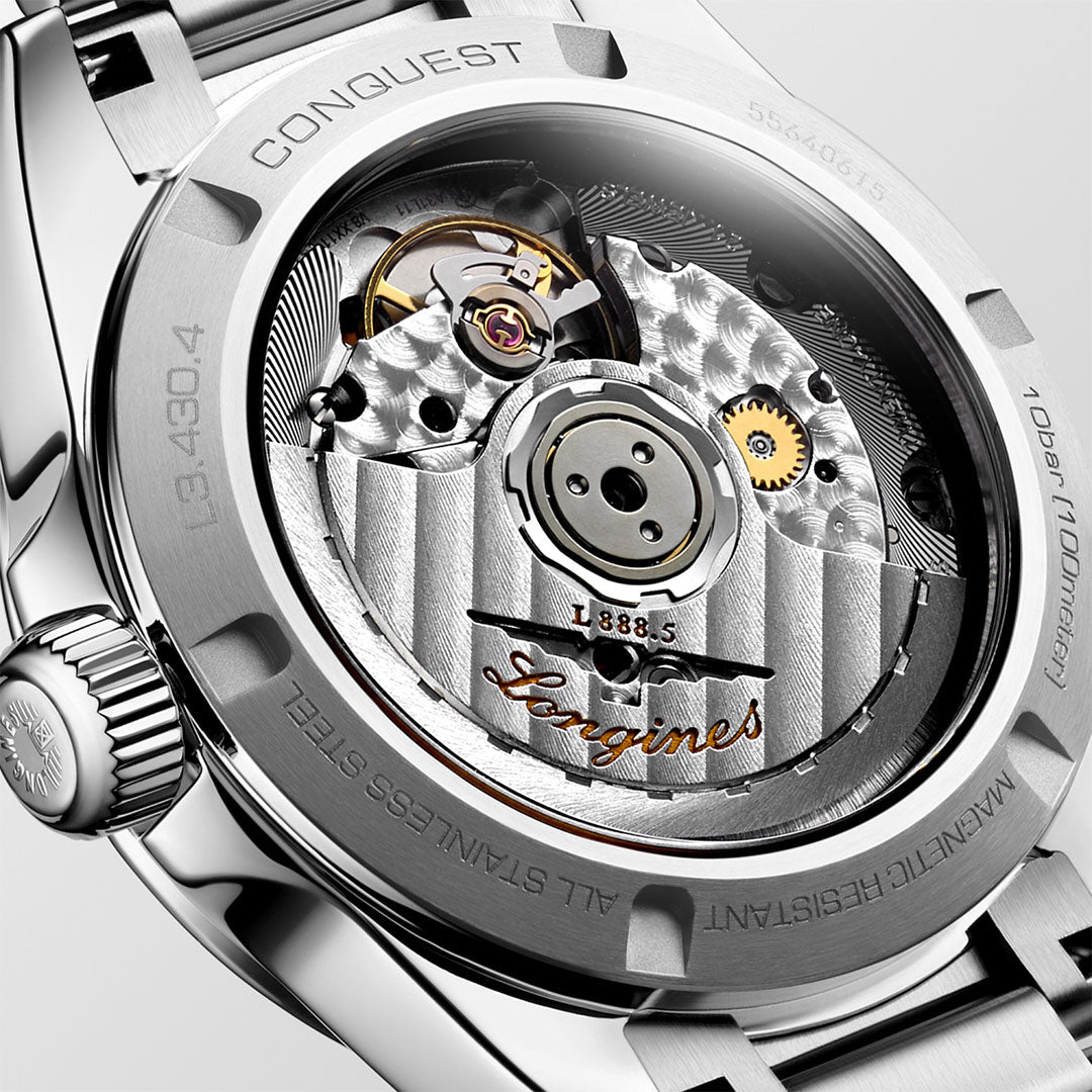 Close-up of the Longines Conquest Automatic 34mm Watch's back reveals its intricate mechanical movement. The stainless steel case exudes elegance with engraved text, while visible gears and components create a detailed, technical appearance. The Longines brand name is prominently displayed on the mechanism, epitomizing timeless performance.