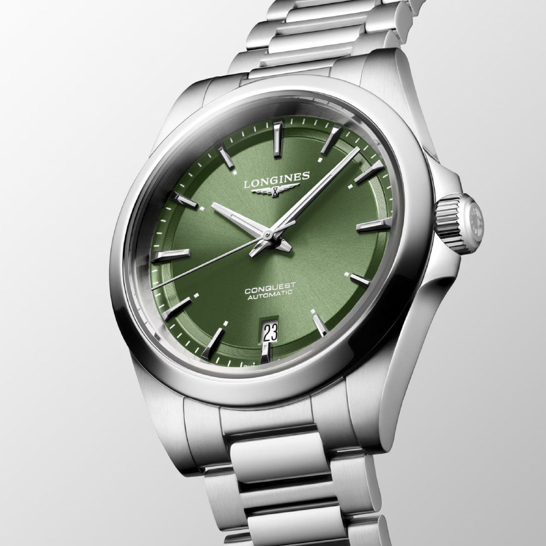 The Longines Conquest Automatic 38mm Watch features a green dial, Swiss Super-LumiNova® silver markers and hands, date at 6 o’clock, and a stainless steel bracelet, shown against a light grey background.