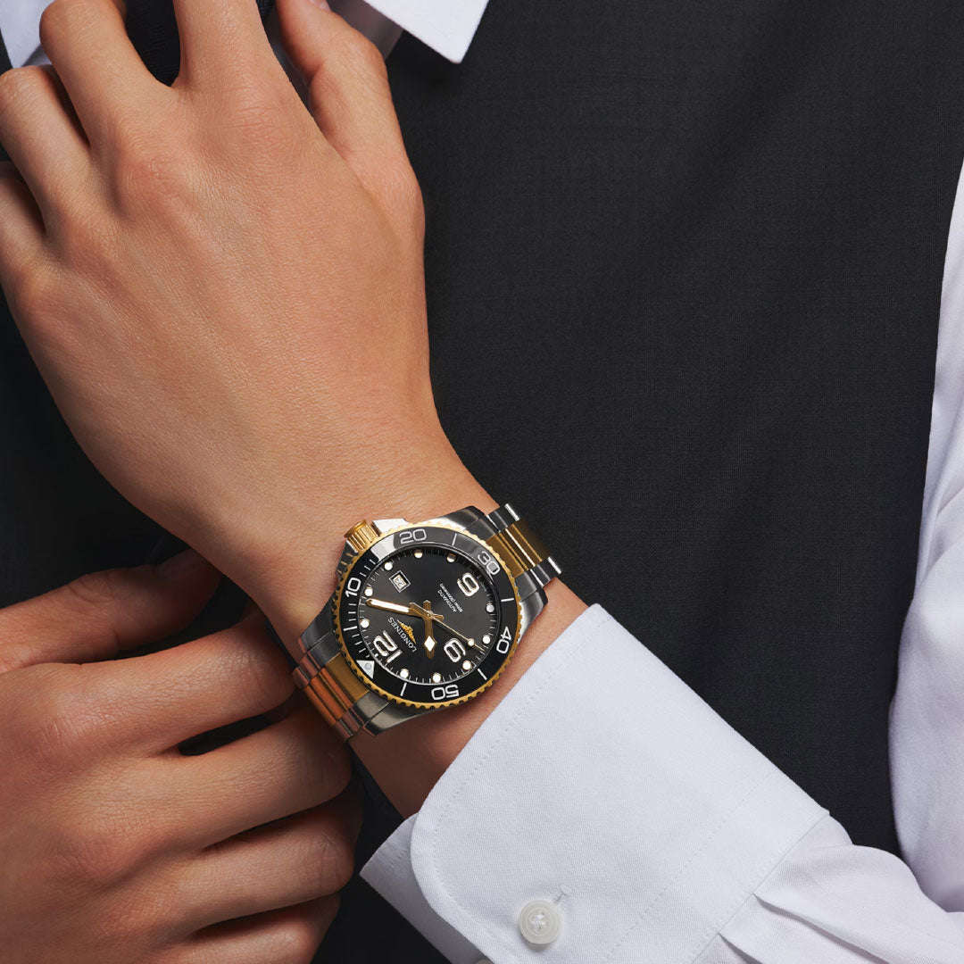 A person in a white shirt and dark vest adjusts their cuff, displaying the Longines Hydroconquest Automatic 43mm Watch with a black dial and unidirectional rotating bezel.