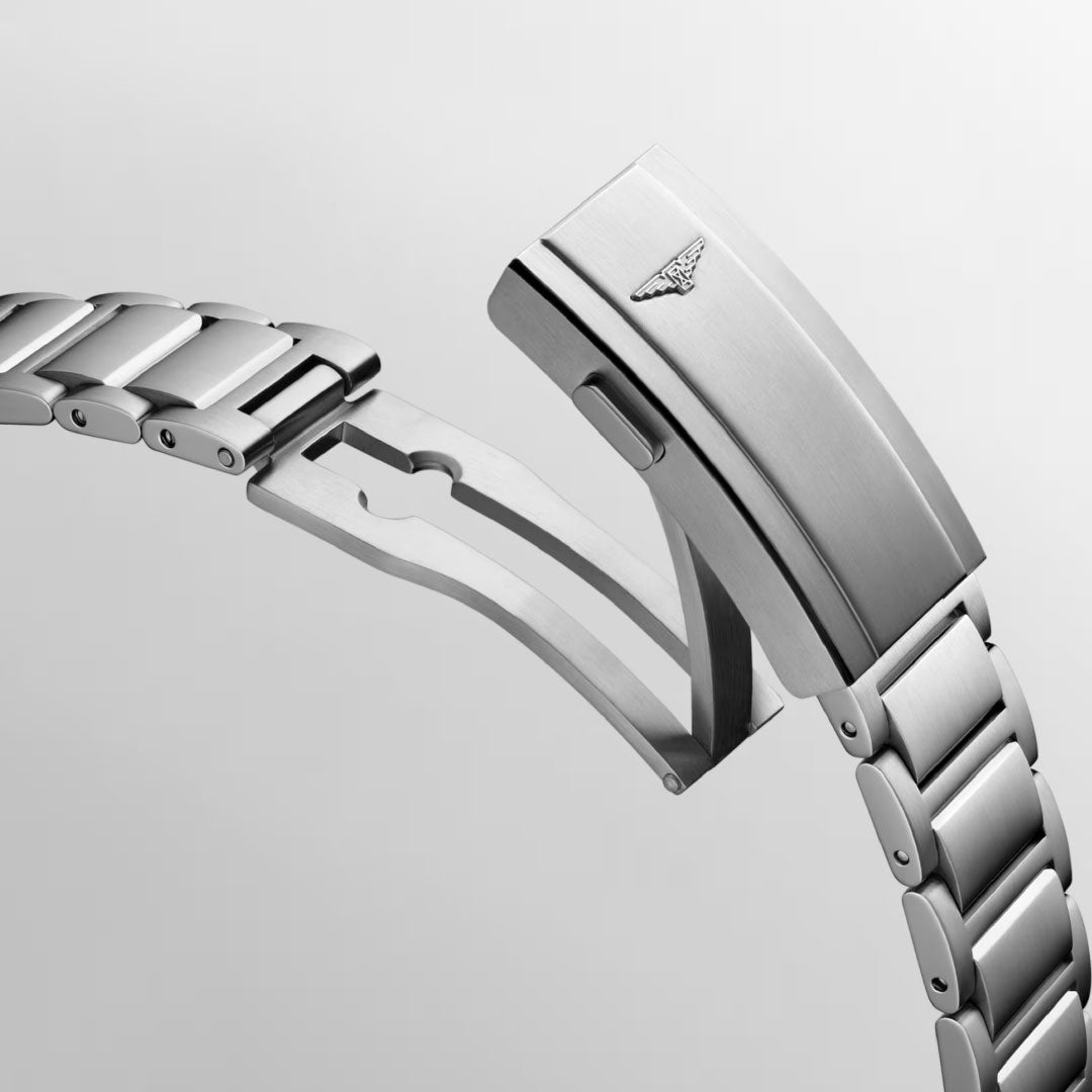 A close-up image showcases the stainless steel bracelet of the Longines HydroConquest Automatic 41mm Watch, featuring a folding clasp mechanism adorned with a subtle, embossed logo of a stylized wing emblem. The background is set against a neutral gray.