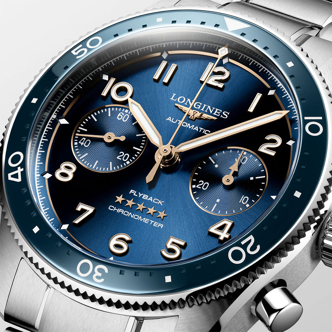 Close-up of the Longines Spirit Flyback Automatic Chronograph 42mm Watch, featuring a blue dial, gold numerals, and two subdials. The metallic bezel with minute markings highlights the words "Flyback Chronometer" and "Automatic," capturing the timeless elegance of the Longines brand.