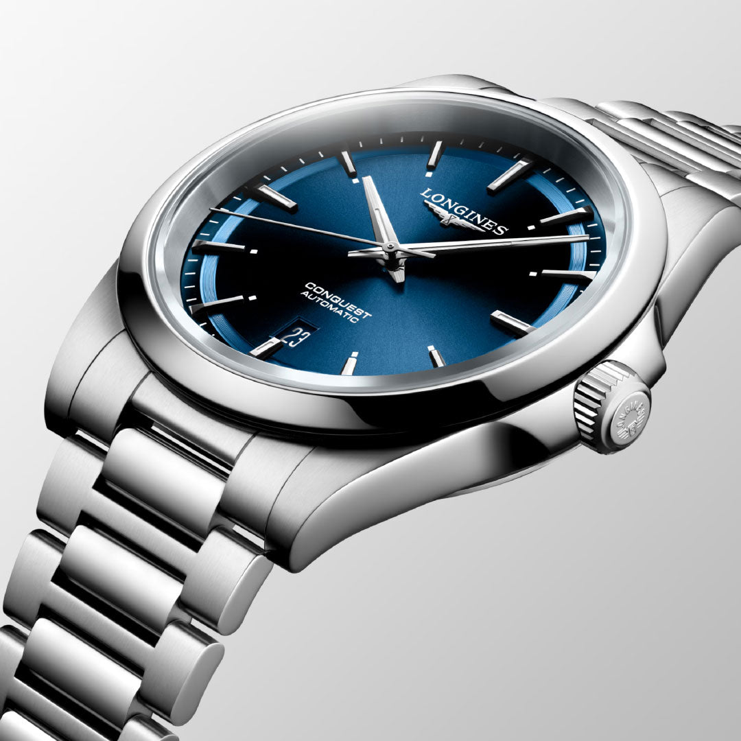 A close-up of the Longines Conquest Automatic 41mm Watch reveals its sophisticated silver metal band and striking blue dial, radiating elegance. With a date display set against a light gray gradient background, this watch epitomizes exceptional performance.