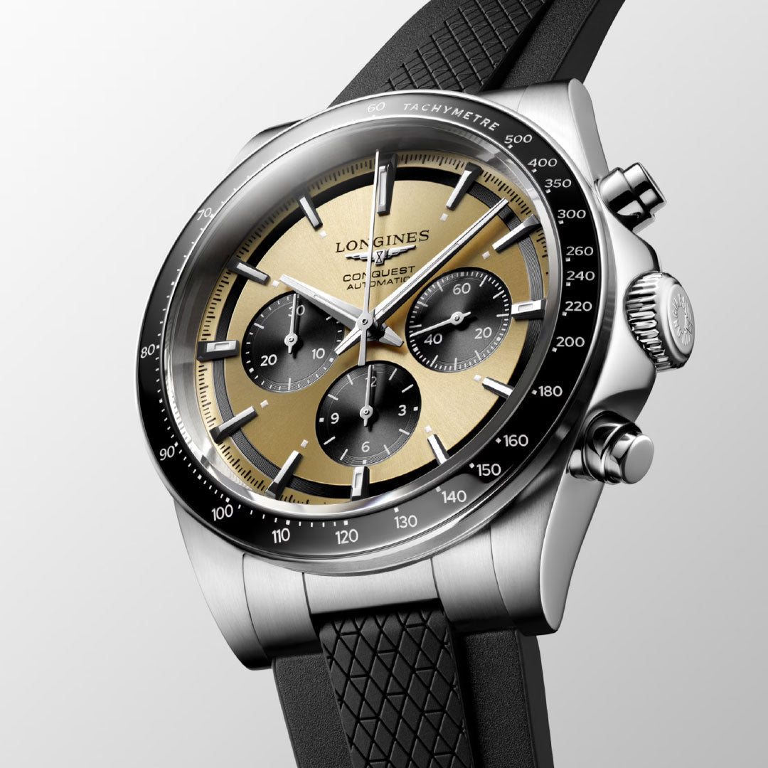 A close-up of the Longines Conquest Chronograph Automatic 42mm Watch, featuring a two-tone gold and black dial, self-winding movement, three subdials, tachymeter scale, stainless steel case, and black textured rubber strap.