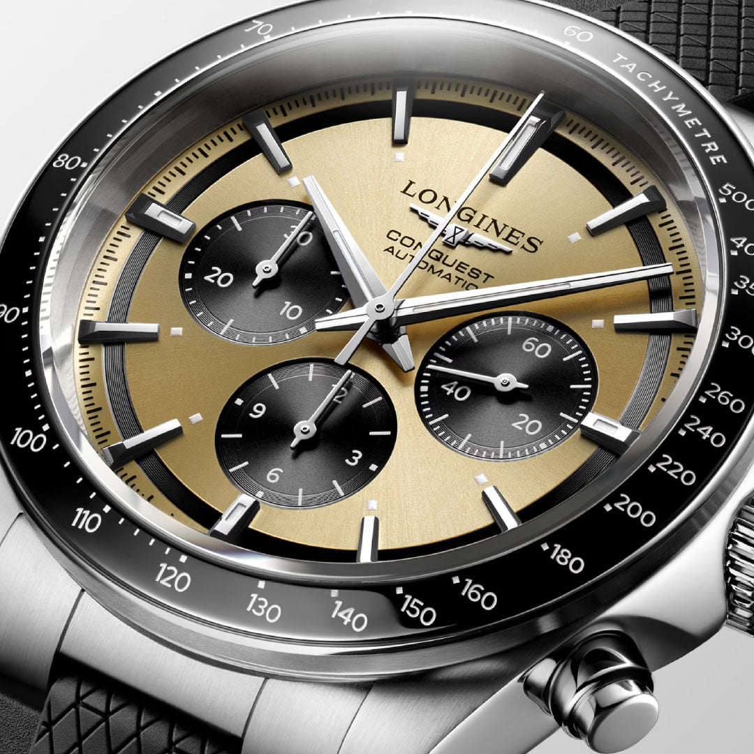 Close-up of the Longines Conquest Chronograph Automatic 42mm Watch by Longines, featuring a gold and black dial, three sub-dials, silver hands, a black tachymeter bezel, and a textured black strap.