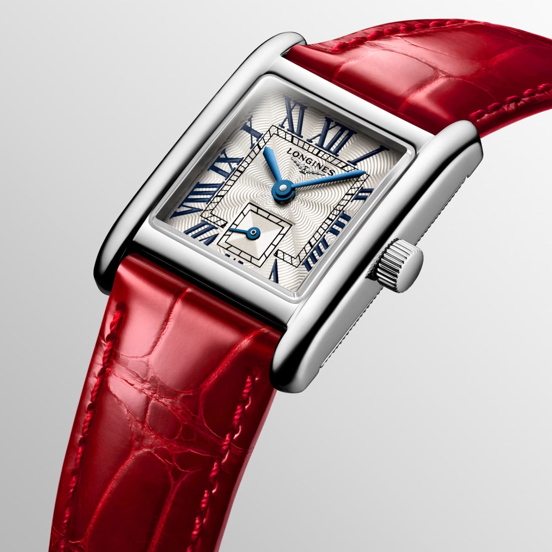 The Longines Mini Dolcevita Quartz 21.5 x 29mm watch features a rectangular stainless steel case and a textured white dial accented by sophisticated blue Roman numerals and hands. It is elegantly paired with a shiny red leather strap, showcasing the "Longines" brand prominently on the face.