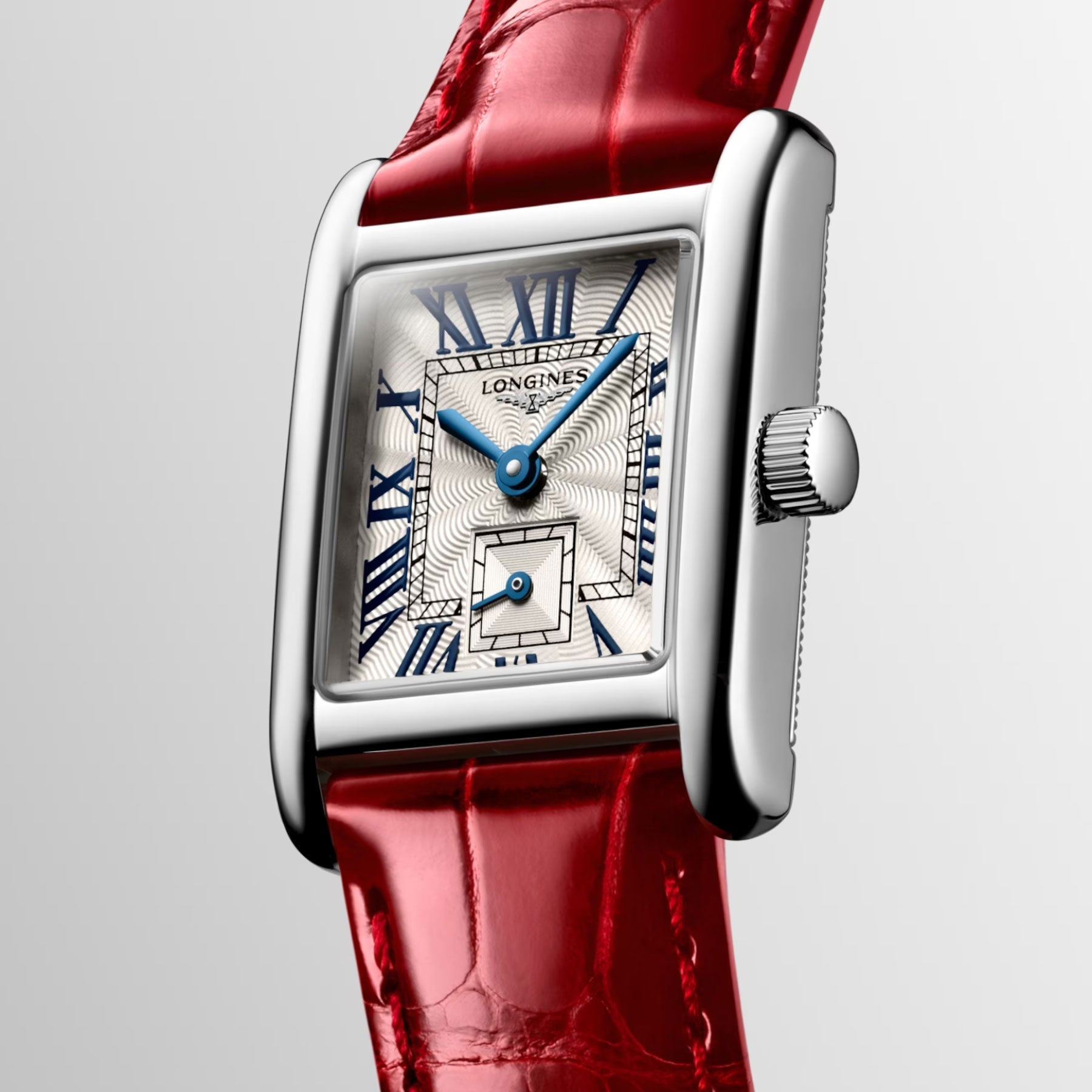 The Longines Mini Dolcevita Quartz 21.5 x 29mm Watch features a rectangular stainless steel case paired with a red leather strap for a stylish appeal. Its watch face is adorned with Roman numerals, complemented by blue hands and intricate detailing, while the crown is conveniently positioned on the right side of the case for easy adjustment.